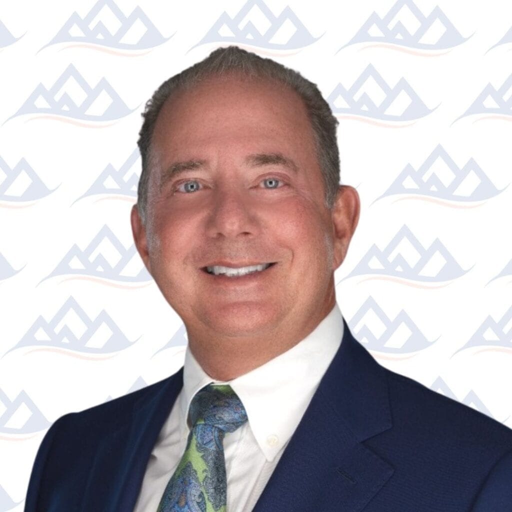 Smiling certified addiction professional in a blue suit, white shirt, and patterned tie, standing in front of a white background with a faint repeating mountain logo—proudly representing our team.