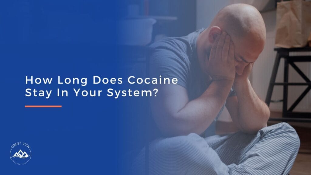 A distressed man sits on the floor with his head in his hands. Text on a blue overlay reads: How Long Does Cocaine Stay In Your System or Urine? A small Crest View Recovery Center logo appears in the corner.