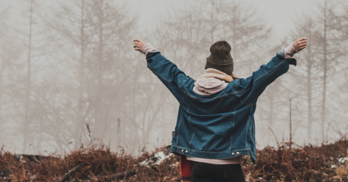 woman in nature in cold weather, back to camera, arms outstretched, celebrating her recovery