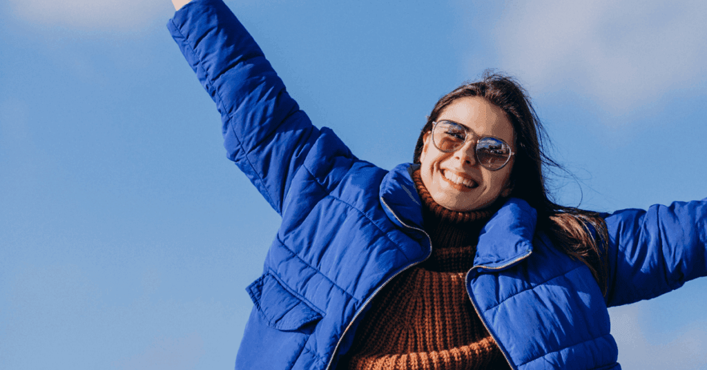 Woman in blue coat and sunglasses, arms wide, ready to start her February recovery journey.
