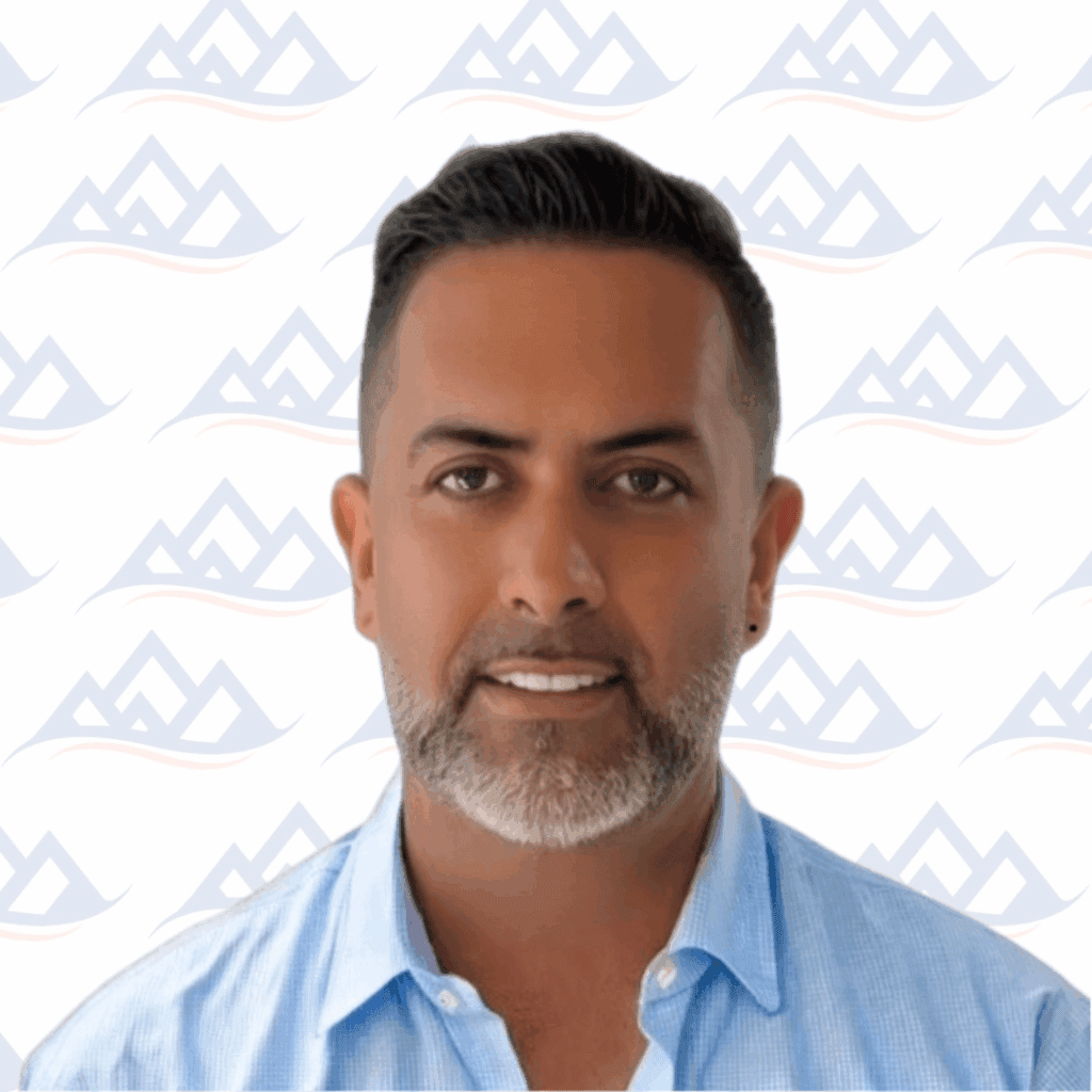 A certified addiction professional with short dark hair and a trimmed beard, wearing a light blue collared shirt, smiles slightly in front of a patterned backdrop with blue and orange mountain-like shapes.