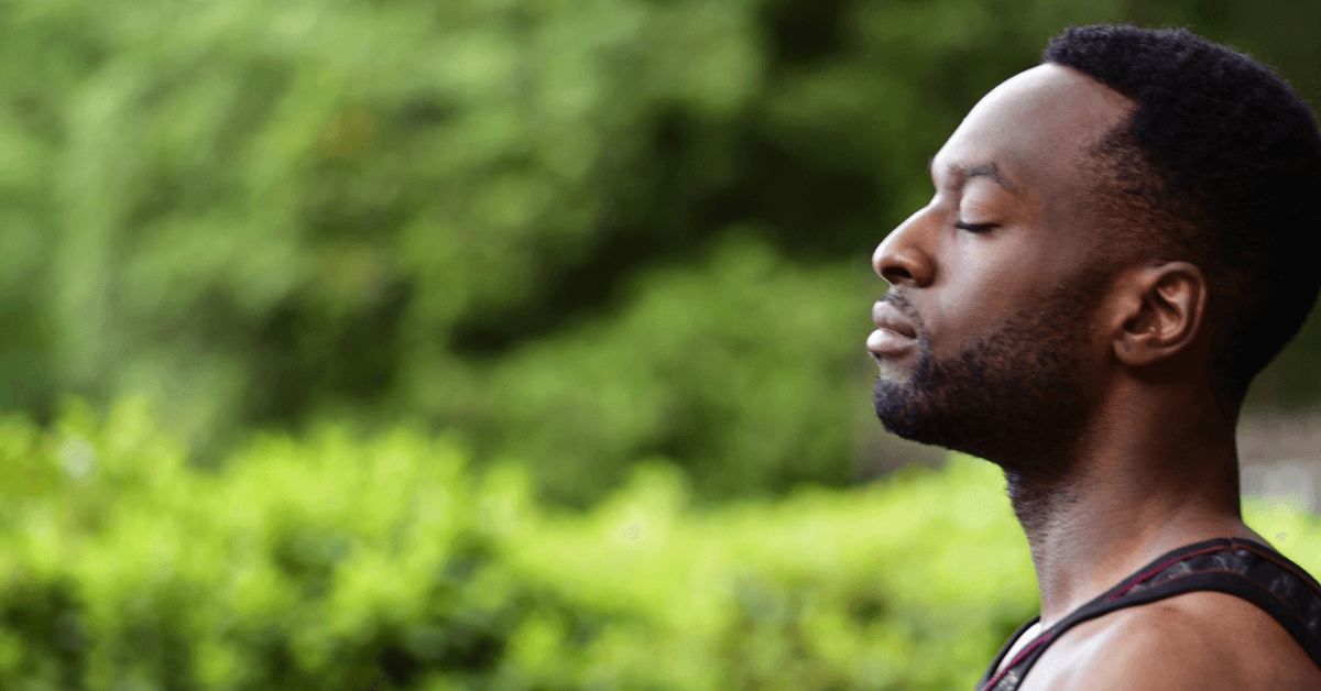 A man in recovery enjoys nature, peacefully closing his eyes with forest scenery in the background.
