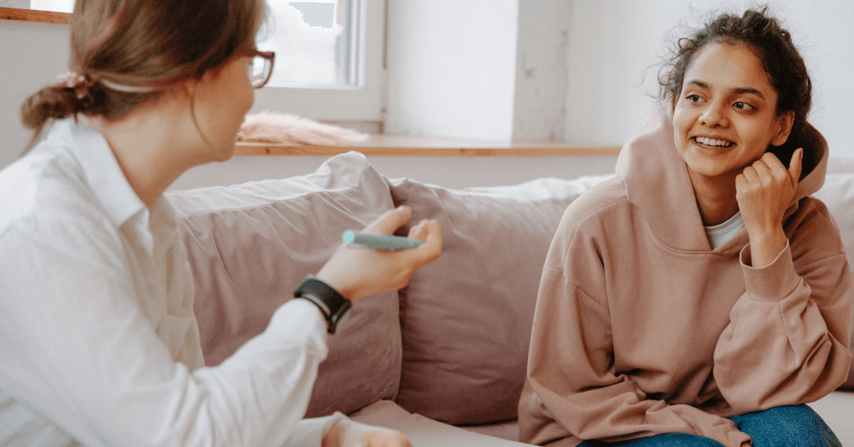 A young woman in recover in a dusty rose pink hoodie speaks with a counselor in a trauma-informed therapy session.