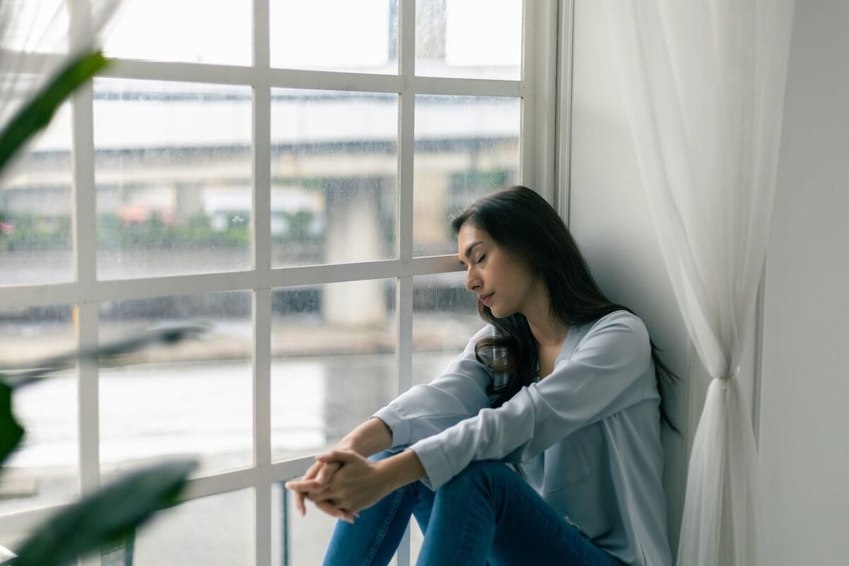 A woman sits by a rain-streaked window, pensive—reflecting the hope found at Crest View Recovery Center in NC addiction treatment.