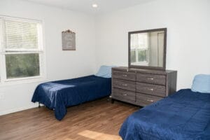 Asheville recovery bedroom with twin beds, blue bedding, dresser, window—comfortable space for outpatient drug rehab clients.