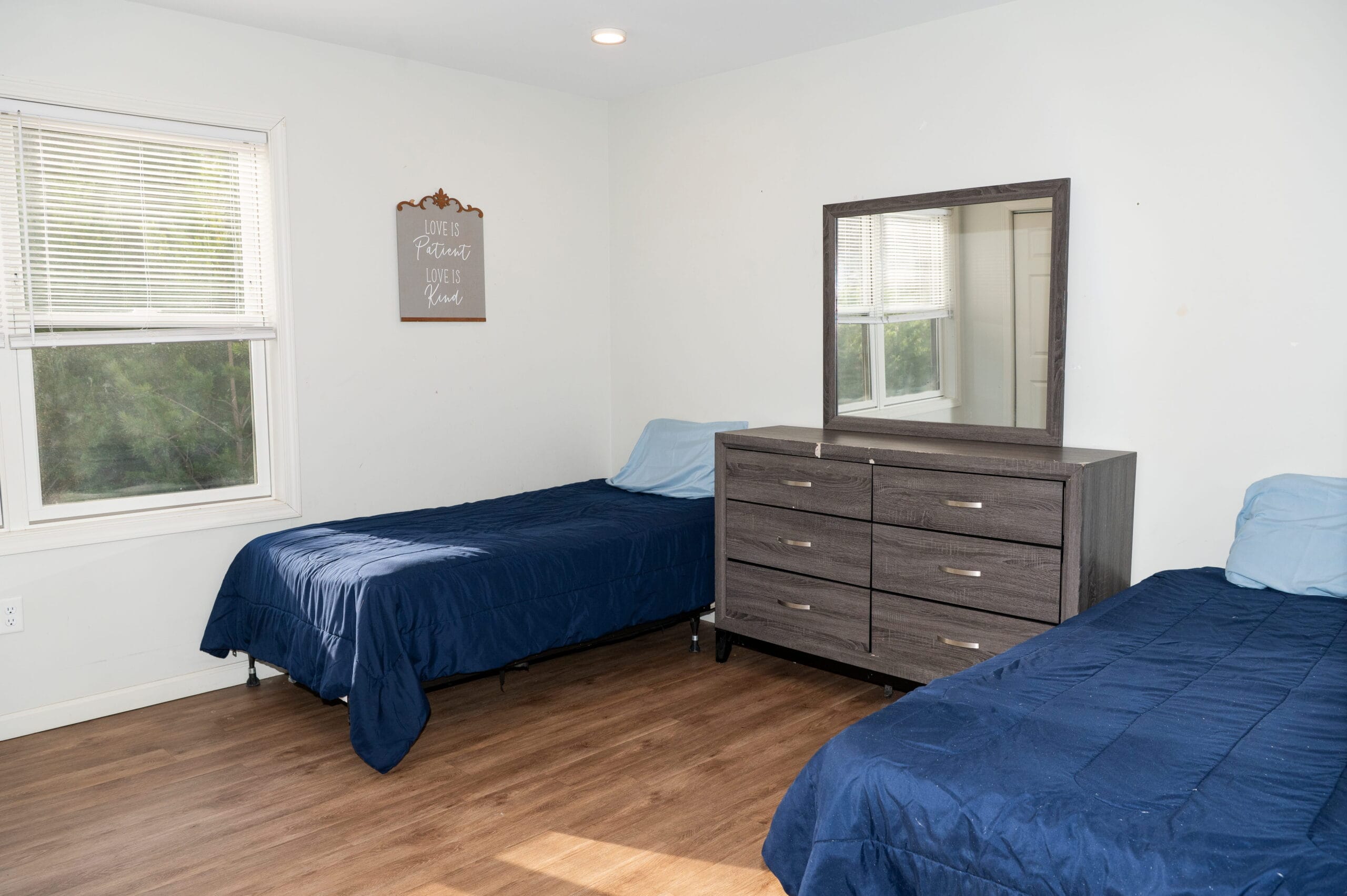 Asheville recovery bedroom with twin beds, blue bedding, dresser, window—comfortable space for outpatient drug rehab clients.