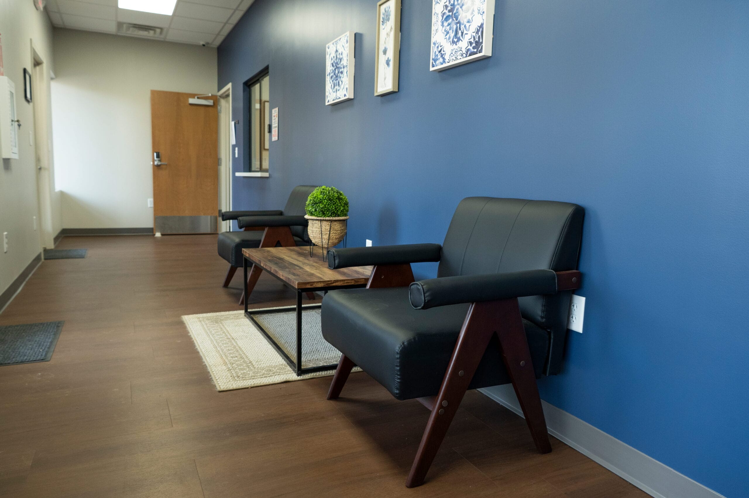 Crest View Recovery Center's Asheville outpatient waiting area with black armchairs, blue walls, art, and a relaxing atmosphere.