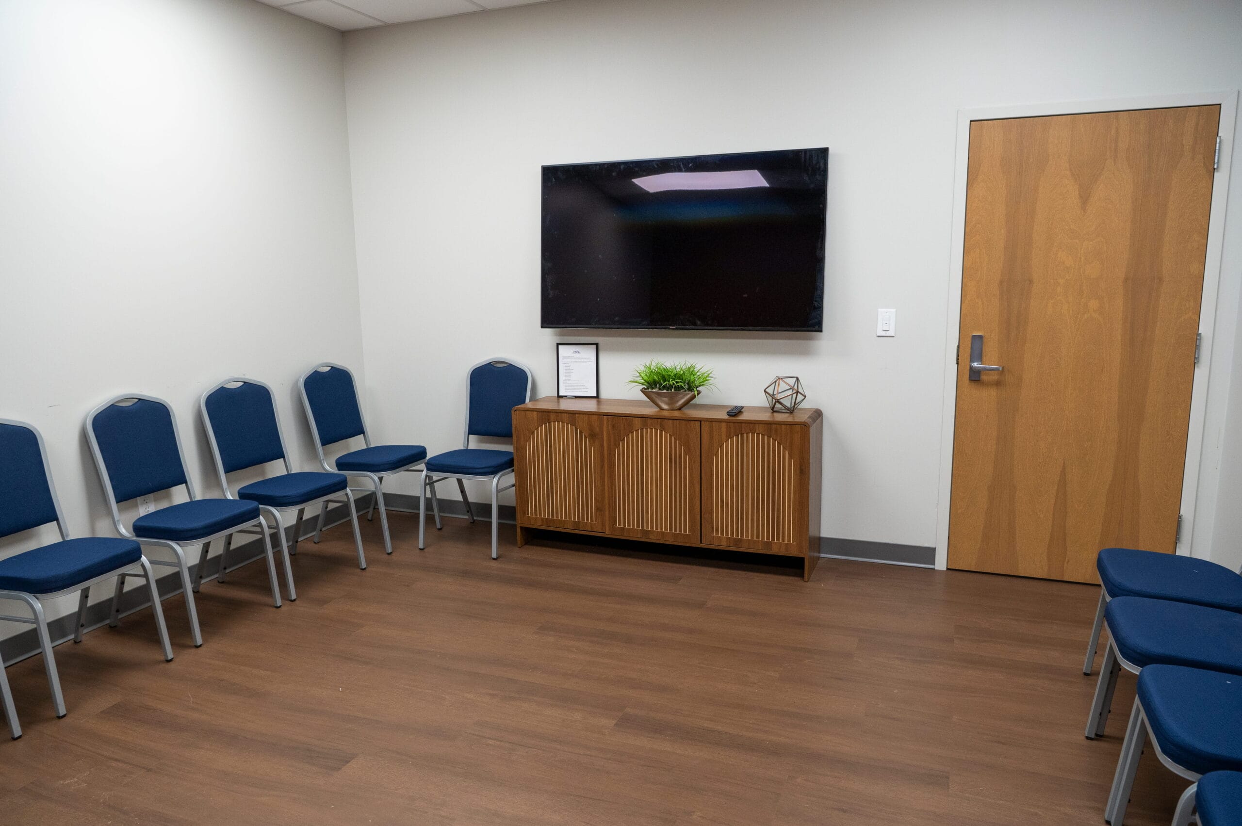 Crest View Recovery Center outpatient waiting room in Asheville, NC with blue chairs, wood floors, TV, décor, and welcoming space.