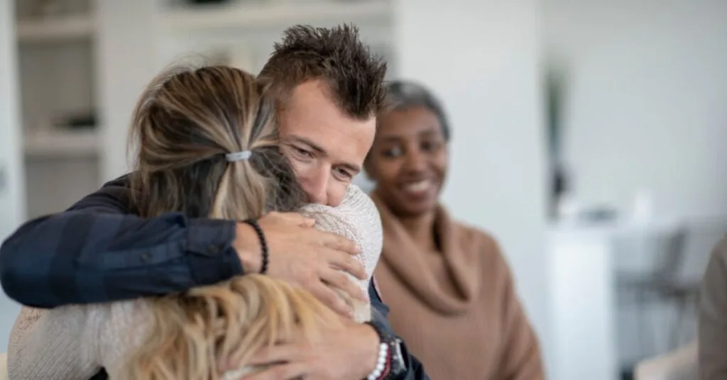In a bright, modern treatment room at Crest View Recovery Center, a compassionate man hugs a woman in recovery while another smiling addiction recovery clinical team member looks on.